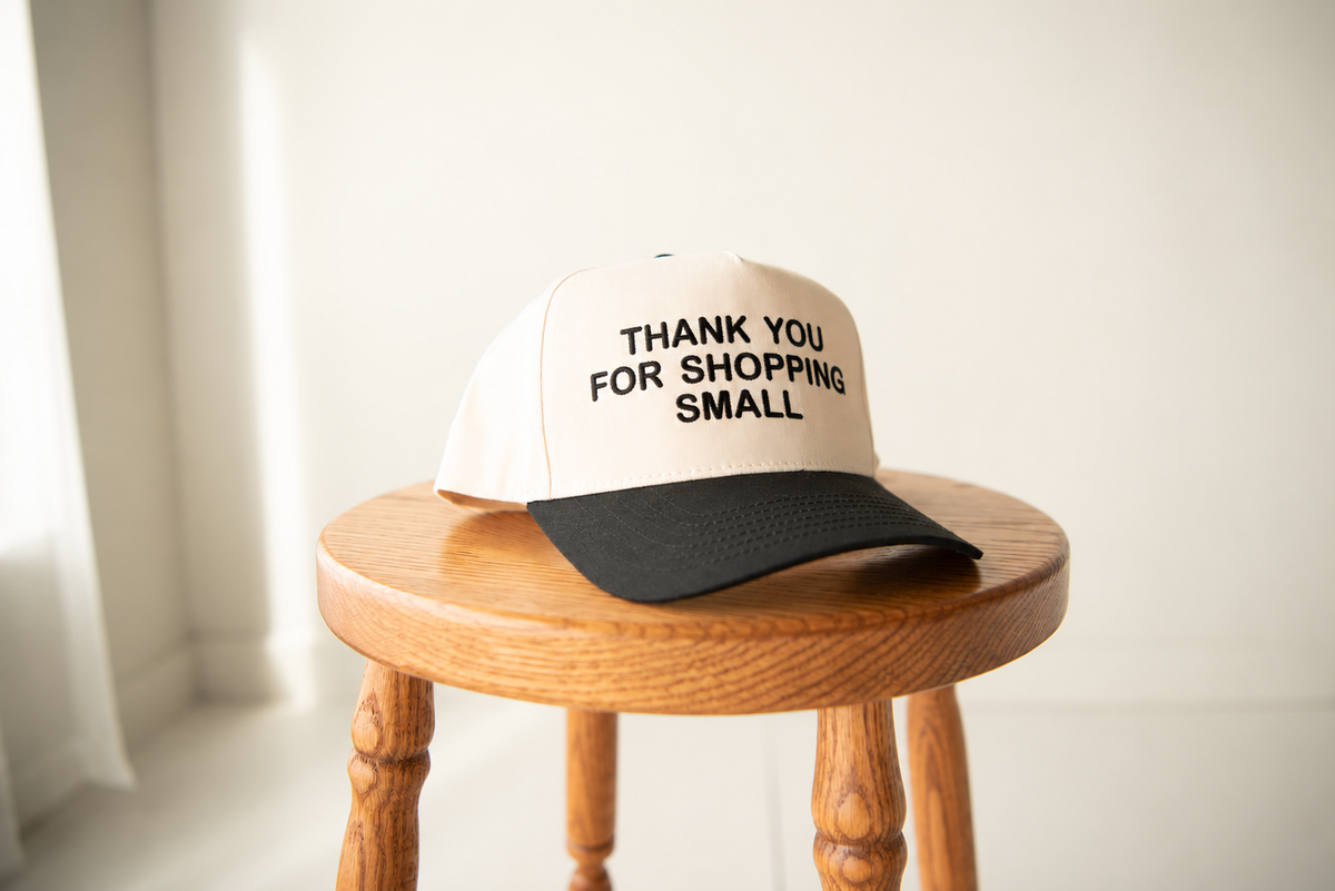 Brand mockup of a cream cap with Thank you for shopping small embroidery on a wooden stool